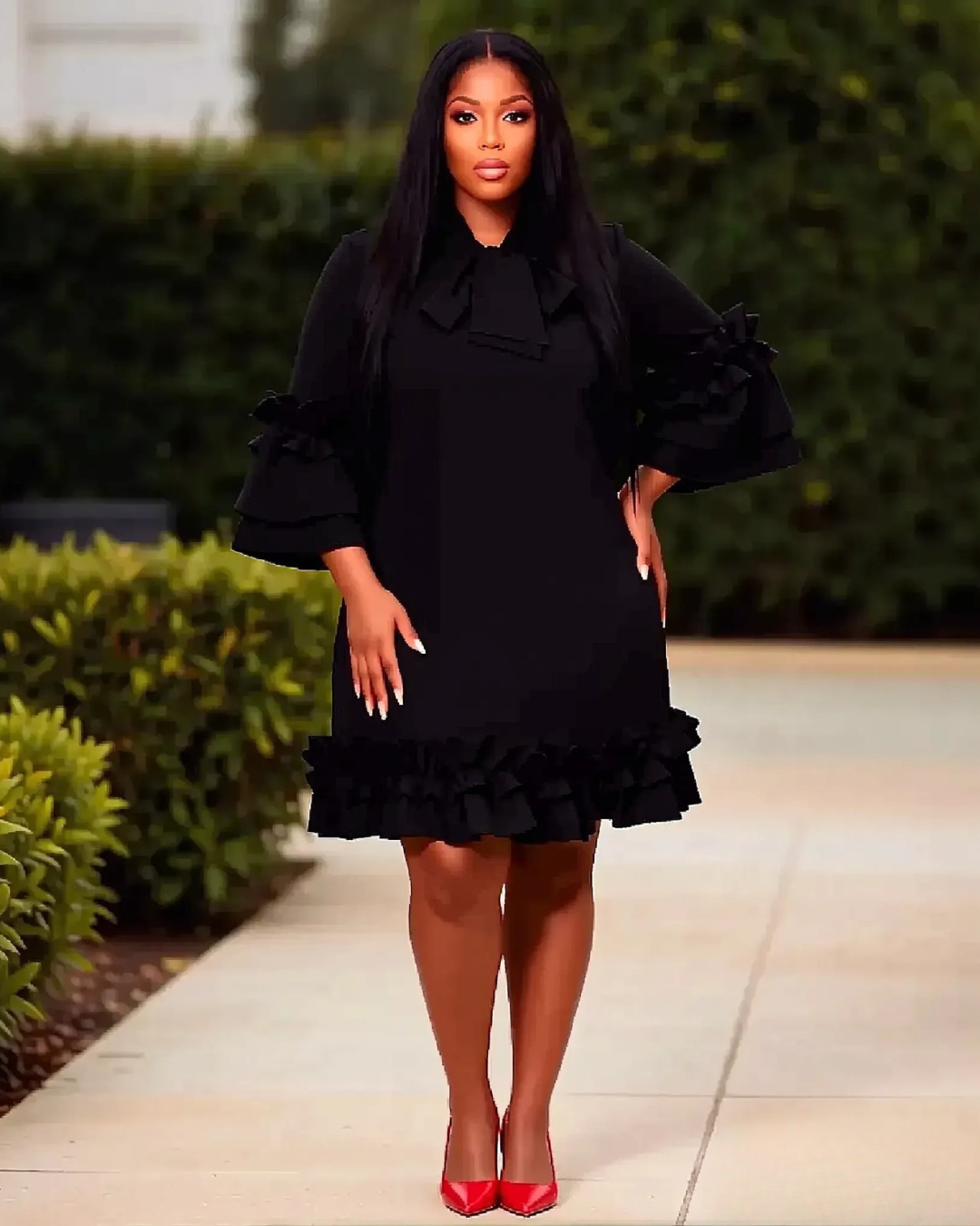 Woman wearing a black dress with ruffled details standing outdoors.