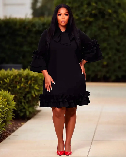 Woman wearing a black dress with ruffled details standing outdoors.